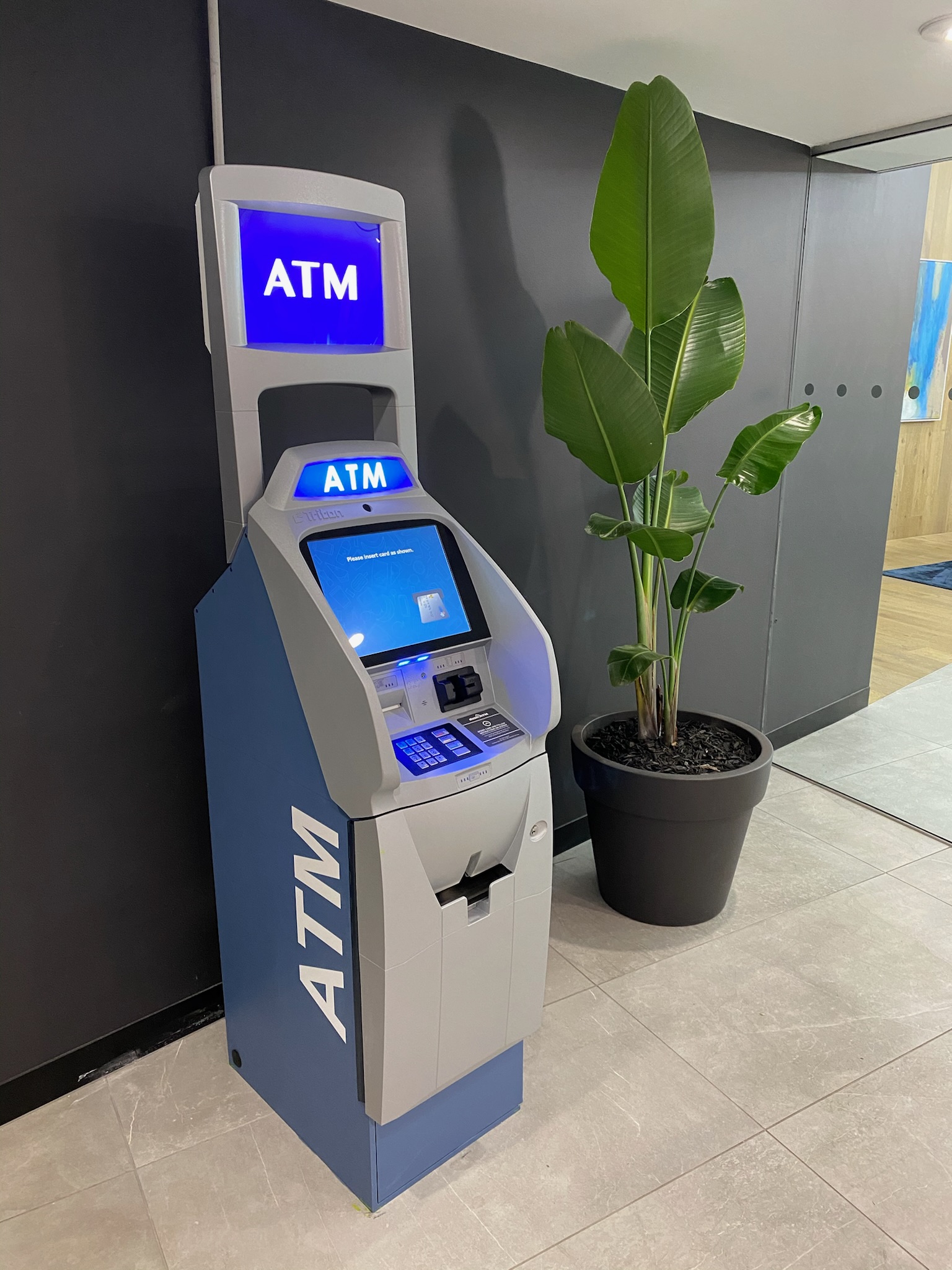 Freestanding ATM installed in a building lobby beside a pot plant